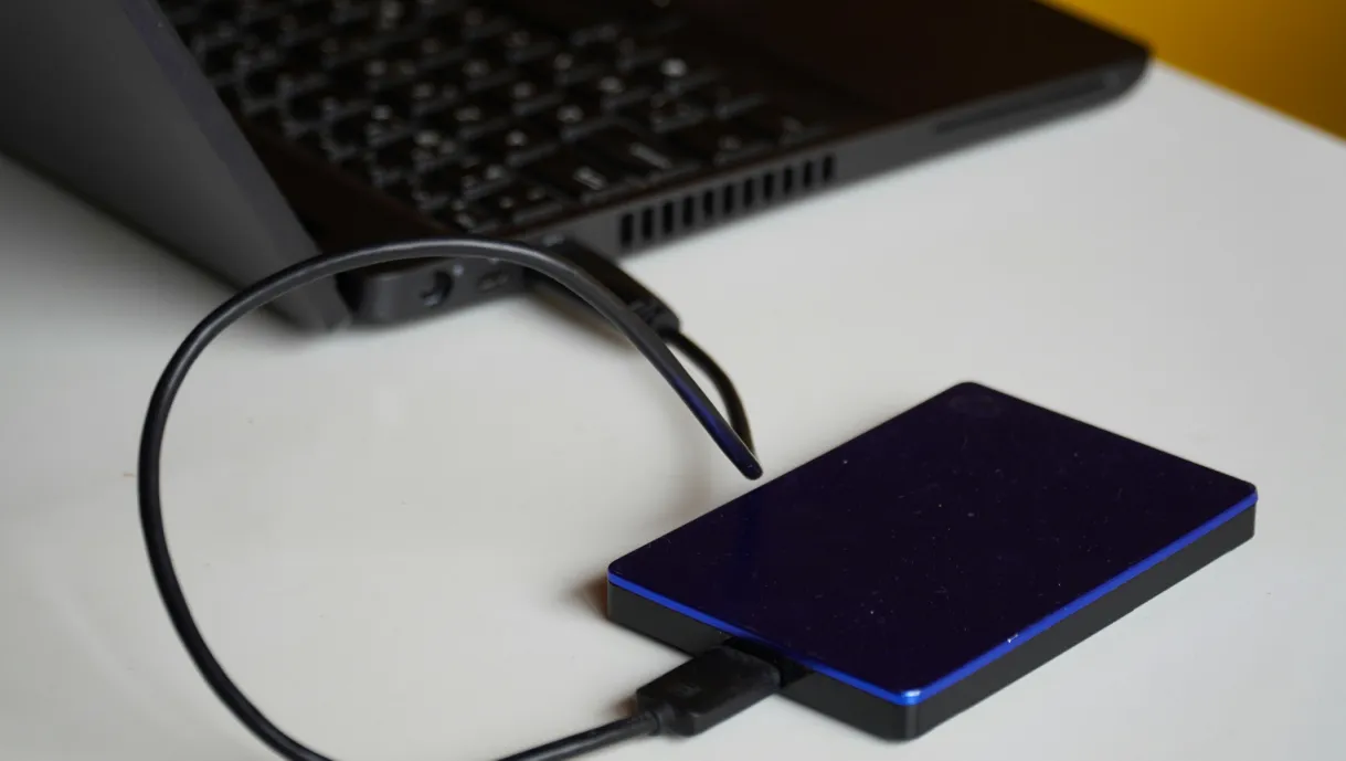 A blue external hard drive connected to a black laptop on a white surface.