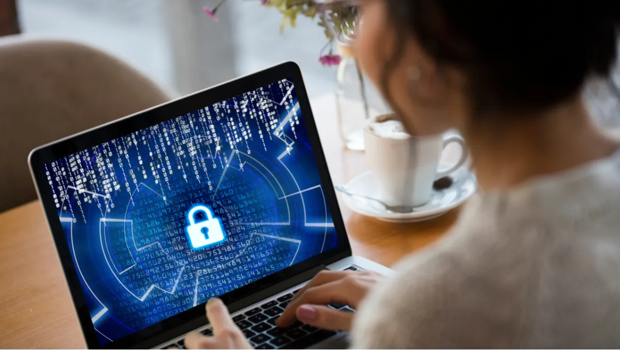 A person uses a laptop displaying a digital padlock symbol, suggesting cybersecurity or data protection.