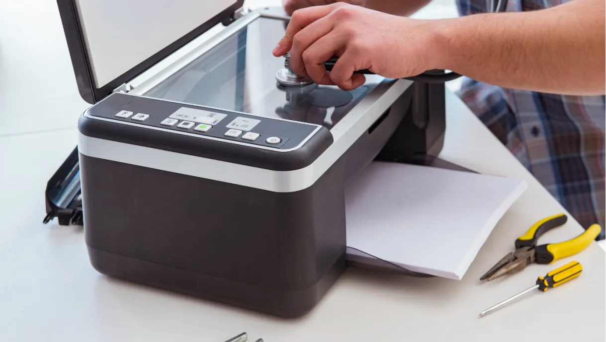 Person repairing a printer-scanner with tools nearby on a white table.