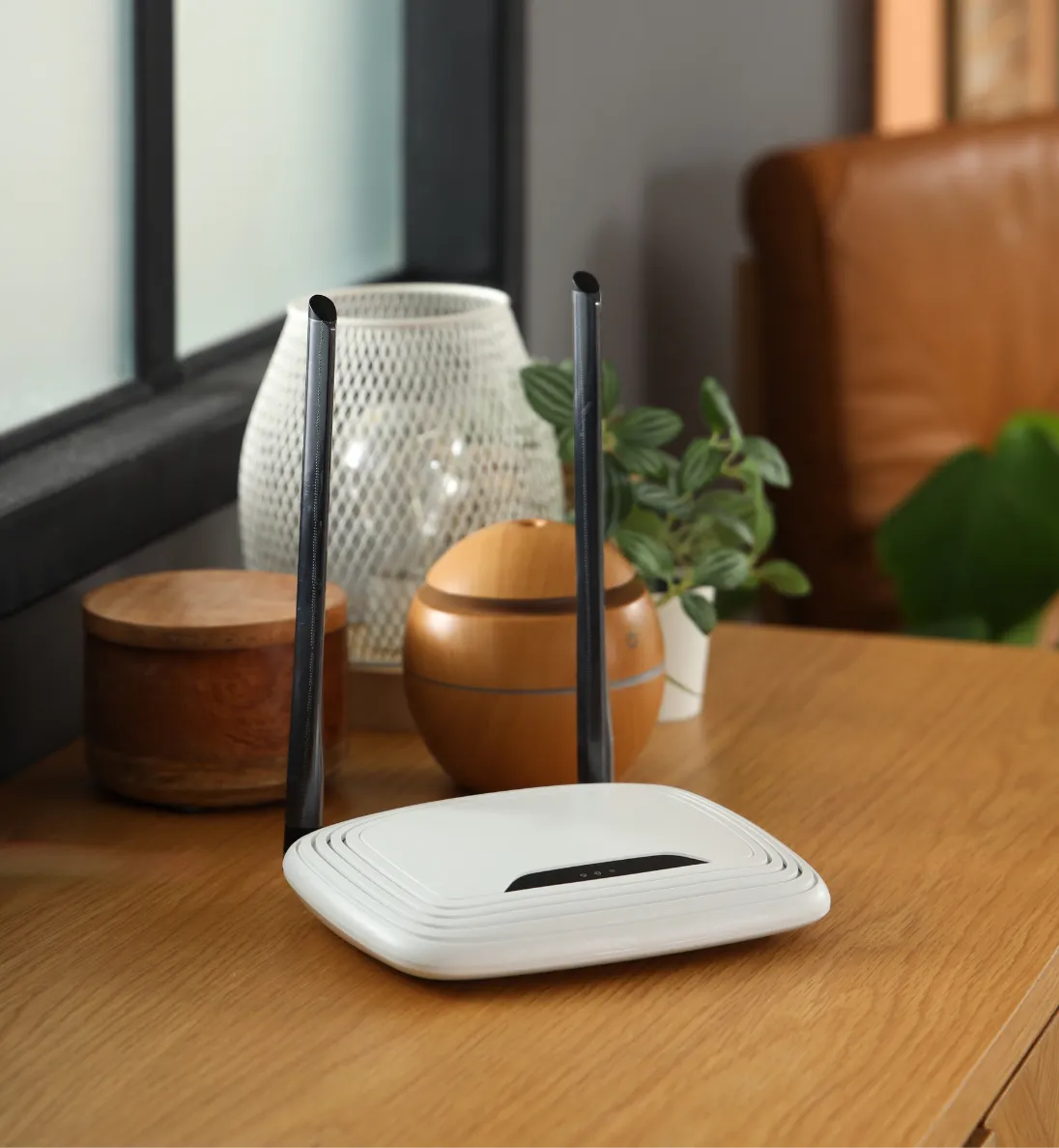home-wifi-1 White Wi-Fi router with two antennas on a wooden table, surrounded by plants and decorative items.