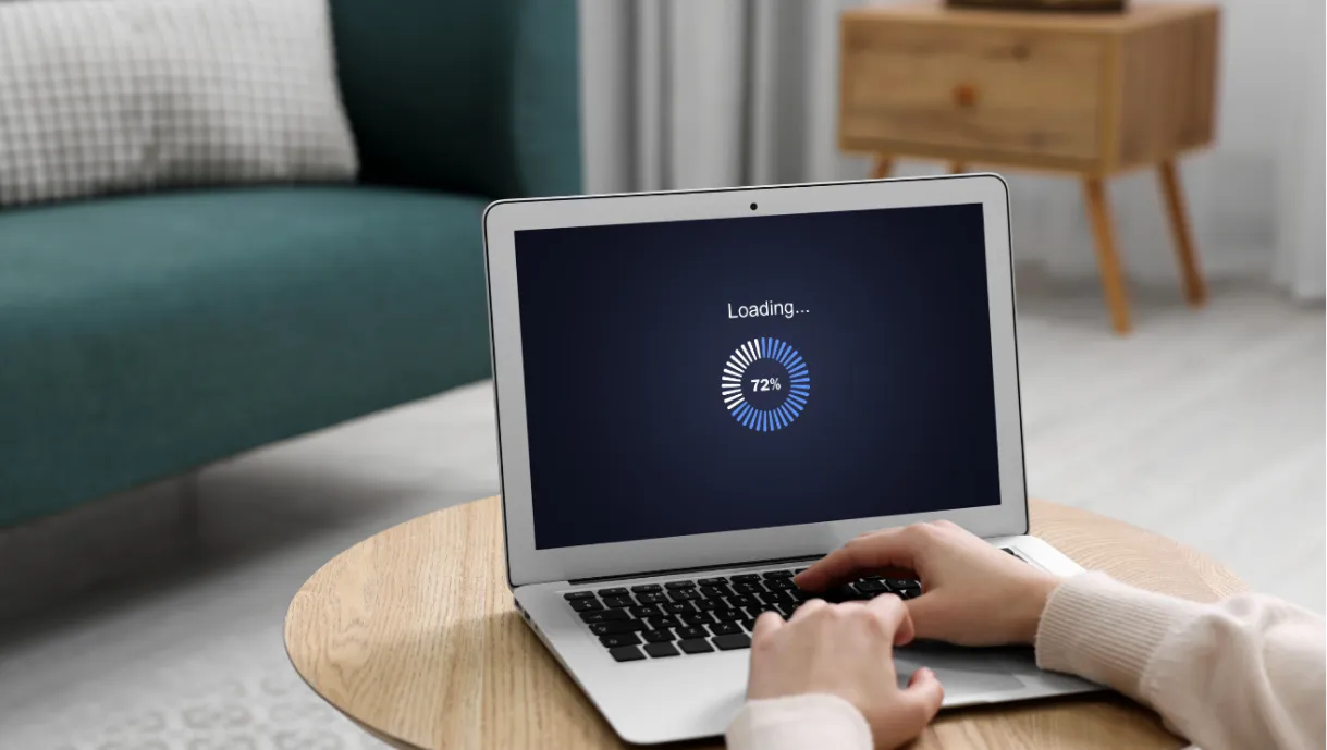 Person using a laptop on a table with a “Loading... 72%” progress bar displayed on the screen.
