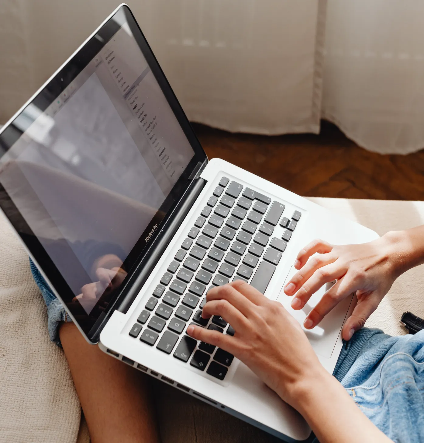 Person typing on a laptop while sitting on a couch, with documents open on the screen.