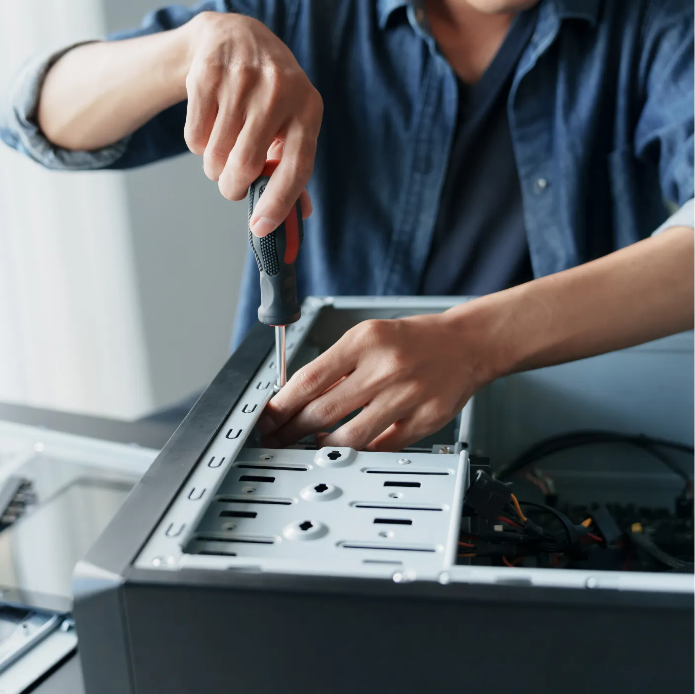 pc-repair-2 Person using a screwdriver to assemble or repair a desktop computer case on a table.