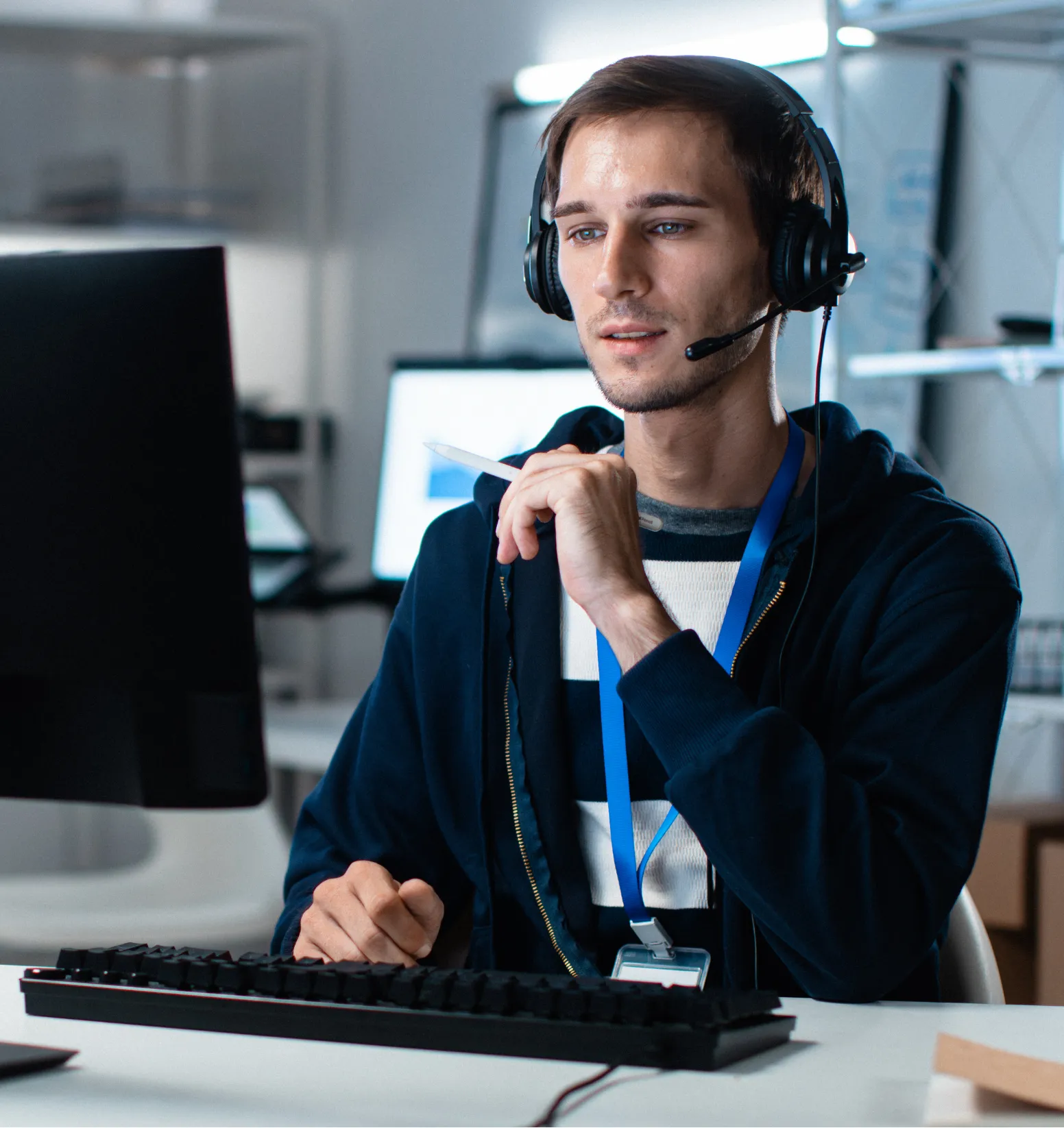 remote-it-1 Man wearing headset and ID badge, sitting at desk using computer in a modern office setting.
