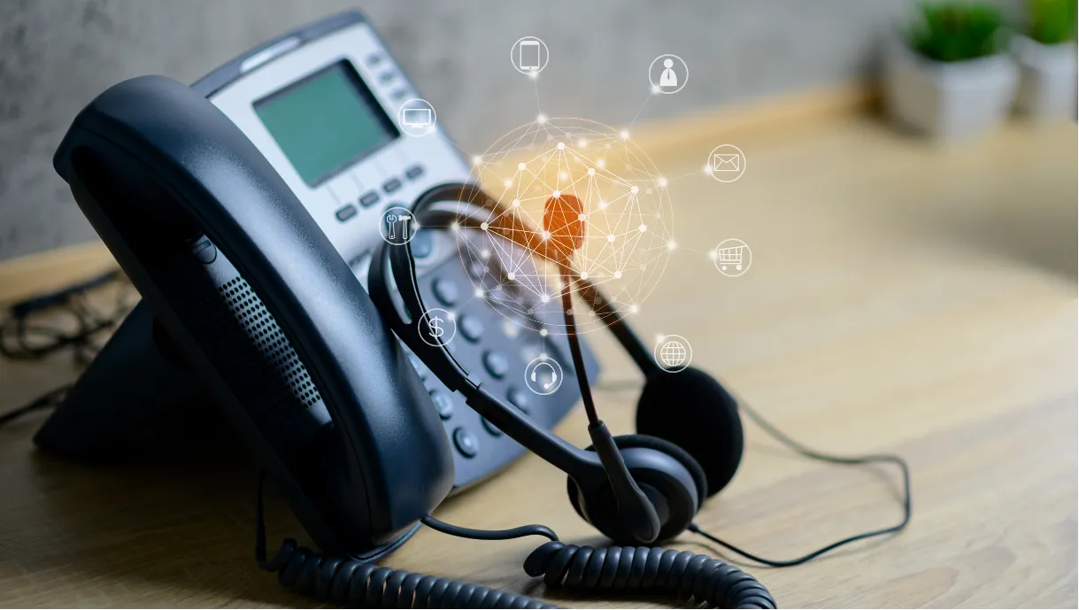 Office desk phone with headset, overlaid with network and communication icons, on a wooden surface.